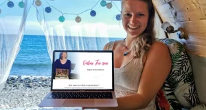 Vroni präsentiert den Laptop mit ihrem Online Business und sitzt im Camper mit Ausblick auf das Meer