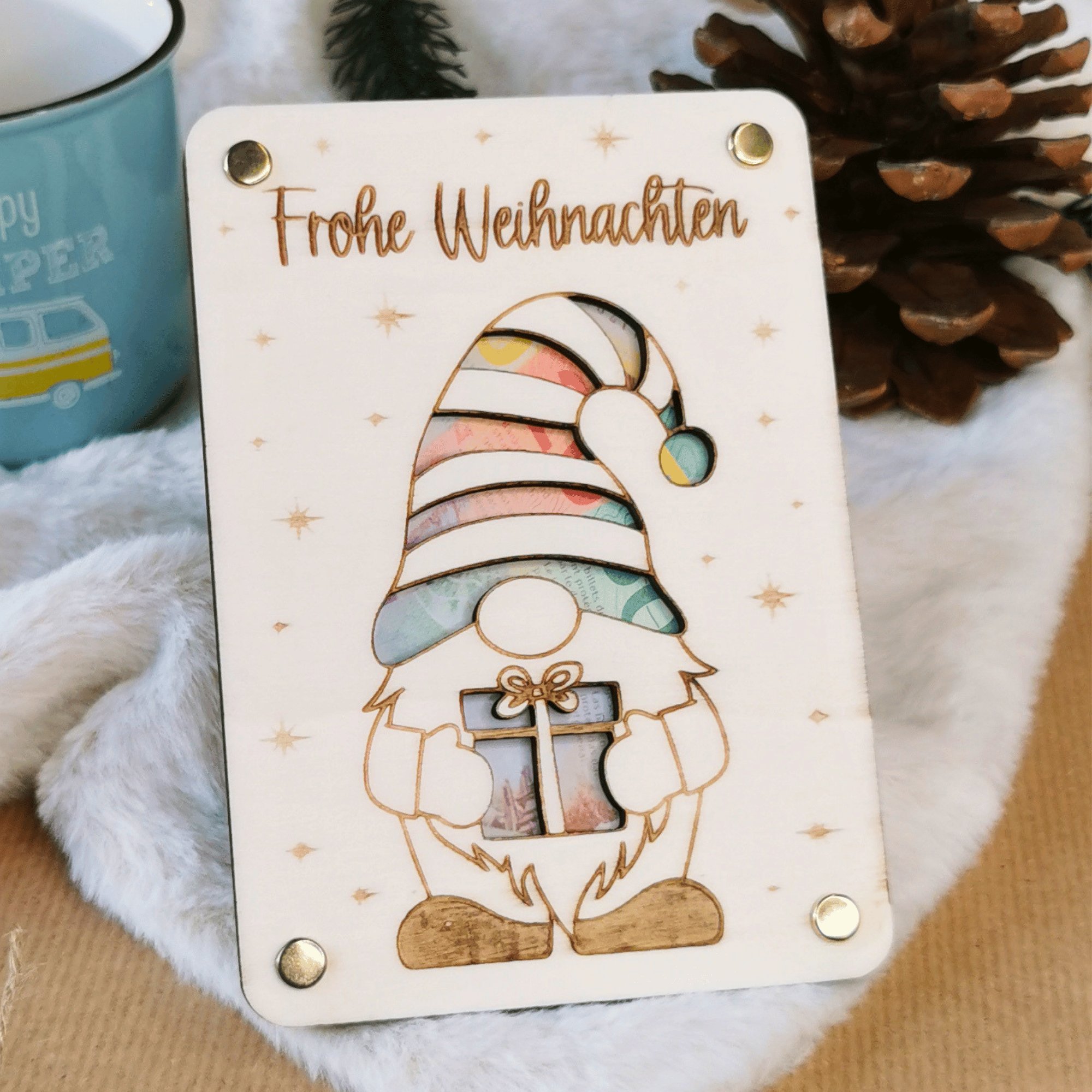 Weihnachts-Gnom Holzkarte mit bunten Geldscheinen hinter der Zipfelmütze, Tannzapfen und blaue Tasse dahinter